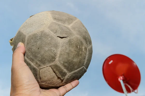 Старый футбольный мяч в руке и красный спутниковый фон — стоковое фото