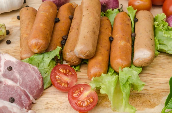 Fresh meat sausages  and vegetables on kitchen board — Stock Photo, Image