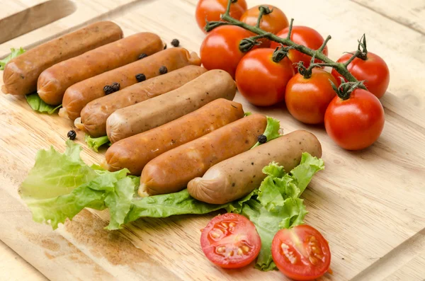 Sausages and tomato on chopping board — Stock Photo, Image