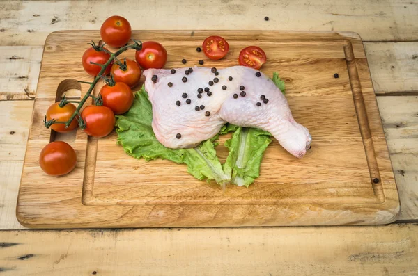 Leg chicken and tomato on chopping board — Stock Photo, Image