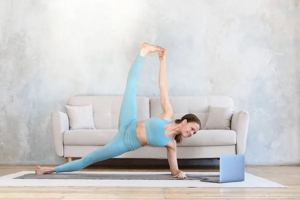 woman goes in for sports online using laptop from home practicing yoga and stretching