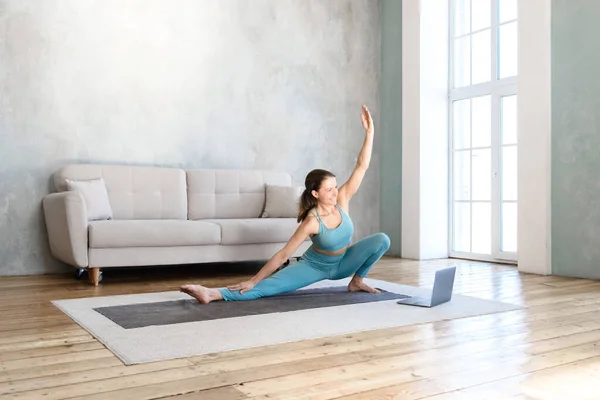 woman doing yoga stretching at home watching video on laptop