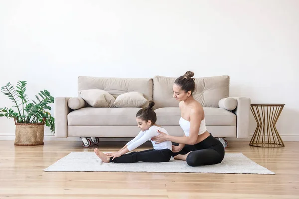 Mom and daughter do yoga stretching gymnastics together at home