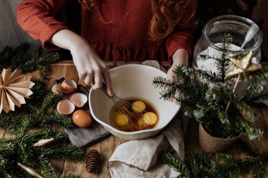 Tahta bir masada, beyaz bir kâsede yumurtaları şekerle çırpıyor..