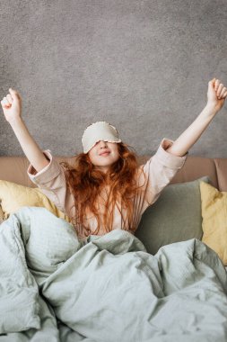 Kızıl saçlı, tüylü kız sabah erkenden yatağında oturuyor..