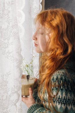 Kızıl saçlı kız sabah kahvesini bardaktan içer..