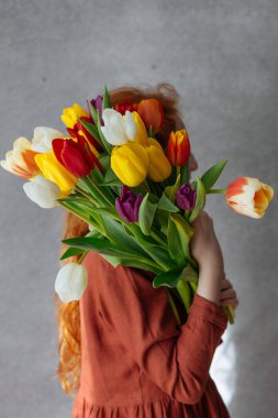 Kızıl saçlı kız elinde bir buket renkli lale tutuyor..