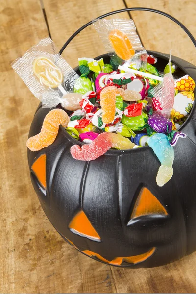 Black plastic pumpkin filled with candy wooden table — Stock Photo, Image