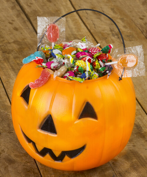 Halloween plastic pumpkin filled with candy on wooden table