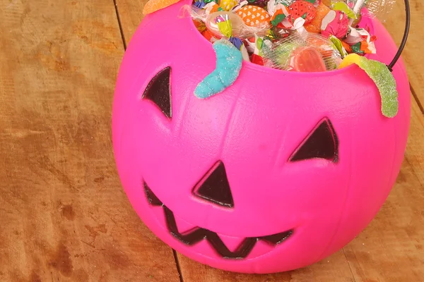 Pink plastic pumpkin filled with candy wooden table — Stock Photo, Image