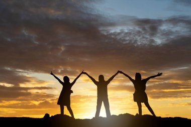 Siluet. Elleri günbatımında duran üç genç insan.