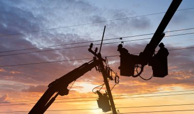 Siluet elektrikçisi yüksek voltajlı aktarım hatlarına kova vagon üzerinde çalışıyor..
