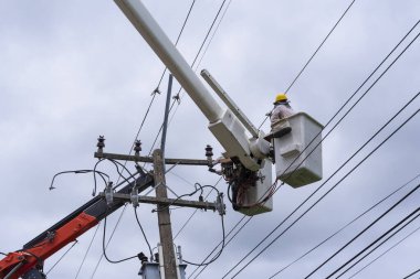 Elektrikçi yüksek voltaj iletim hatlarını korumak için kova vagon üzerinde çalışıyor..