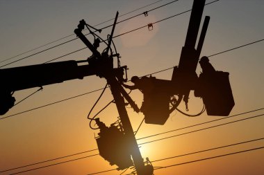 Silüet elektrikçisi yüksek voltaj iletim hatlarını korumak için kova vagon üzerinde çalışıyor..