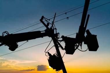Silüet elektrikçisi yüksek voltaj iletim hatlarını korumak için kova vagon üzerinde çalışıyor..