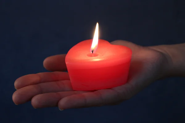 Vela de coração vermelho em uma mão. Luz no escuro — Fotografia de Stock