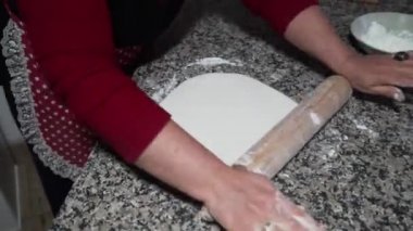 Bir kadın merdaneli baklava hamuru yuvarlıyor.