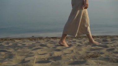 Dişi bacakları ve ayakları kumlu sahilde deniz dalgaları boyunca yürüyor..
