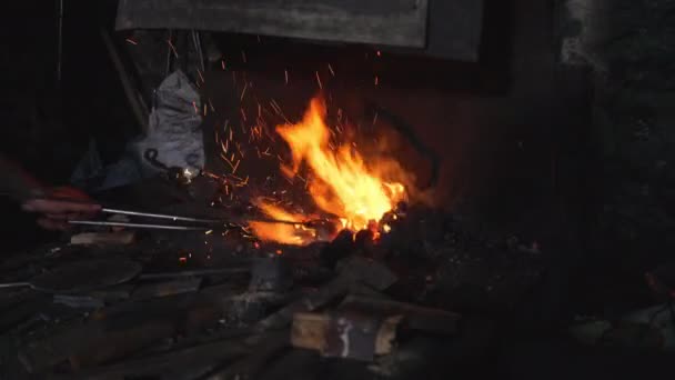 Um ferreiro em chamas aquece o metal para forjar o produto — Vídeo de Stock