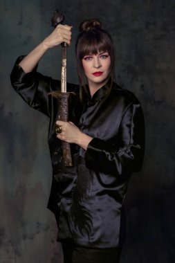 Parlak makyajlı güzel bir kadın. İçinde minimalist bir iç mekan var. Yelpaze ve hançerle.