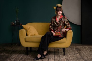 Parlak makyajlı güzel bir kadın. İçinde minimalist bir iç mekan var. Yelpaze ve hançerle.