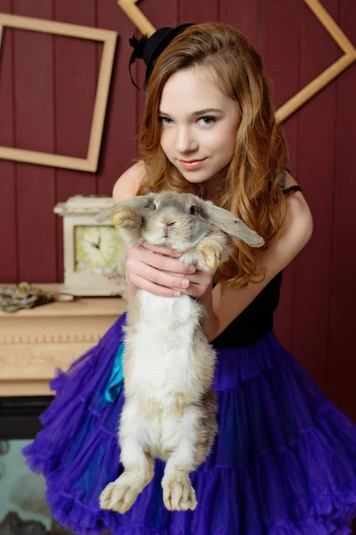 Mladá dívka na obrázku z Alenky v říši divů stojí u krbu a drží králík — Stock fotografie