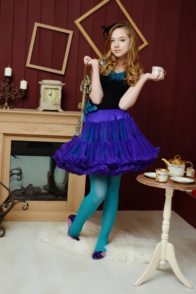 Young girl in the image of Alice in Wonderland stands near the fireplace and holds a bunch of keys and tea cup — Stock Photo, Image