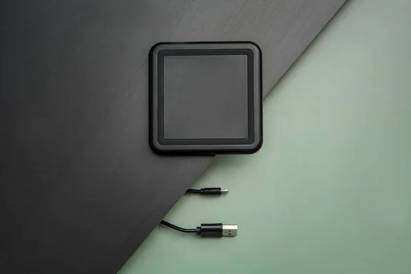 Wireless charger squared and black qi technology on a black wooden table and cable