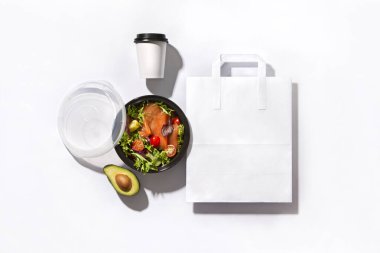 Kimlik ayarlandı. Pakette somon balığı, avokado salatası, kahve fincanı ve beyaz arka planda kağıt torba var.