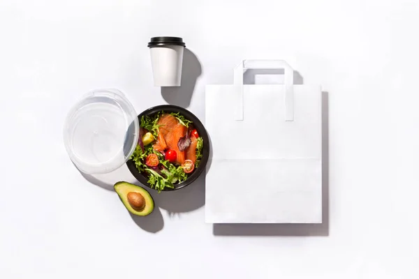 Kimlik ayarlandı. Pakette somon balığı, avokado salatası, kahve fincanı ve beyaz arka planda kağıt torba var.
