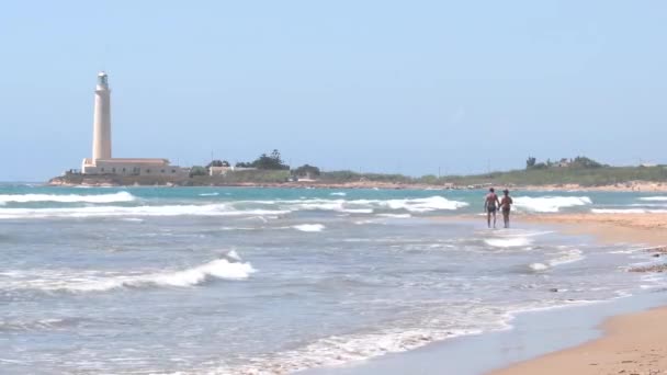 Italiano bela praia na Sicília Casal andando na costa. Farol no fundo — Vídeo de Stock