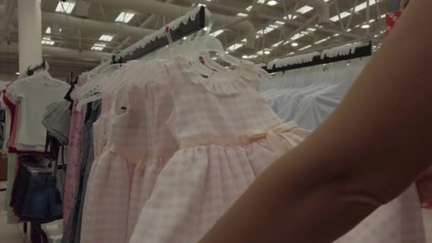 Dziewczyna wybiera sukienkę dla dzieci w sklepie — Wideo stockowe