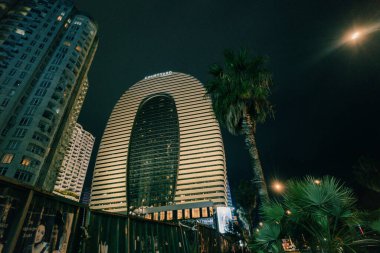 Batumi, Georgia, 7 Ekim 2025. Aydınlatılmış modern binanın su yüzeyine yansıyan gece görüşü. Yüksek kalite fotoğraf