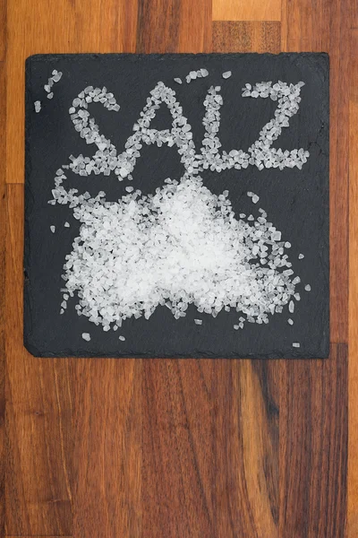 Sól na czarnej płycie z drewnianym tłem — Zdjęcie stockowe