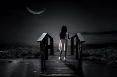 Genç bir kız sabahın erken saatlerinde tahta bir köprüde tek başına duruyor, yarım ay gecesi, yapayalnız..