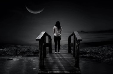 Sabahın karanlığında ahşap bir köprüde duran bir kadın, güzel bir yarım ay gecesi..