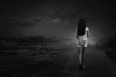 Geceleri çakıllı yolda tek başına yürüyen genç bir kızın siyah beyaz portresi..