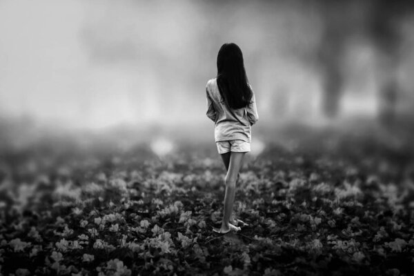 A black and white portrait of a young girl standing alone in the middle of a flower that had fallen from the tree.