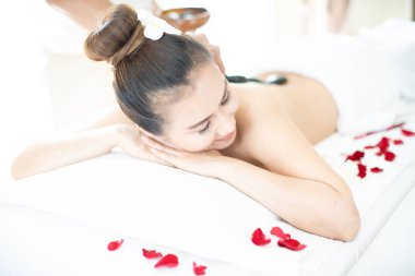 Bir kaplıca masörü Asyalı bir kadının üzerine sıcak taş koyuyor. Rahatlatıcı bir masaj merkezinde uzanmak.