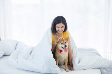 Yatakta Shiba Inu köpeğiyle oturan Asyalı bir kadın..