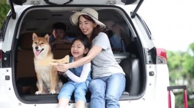 Mutlu bir aile tatile çıkmaya hazırlanıyor. Mutlu Asyalı çocuklar ve Shiba Inu 'lu anne oturuyor ve Sing Song arabada..