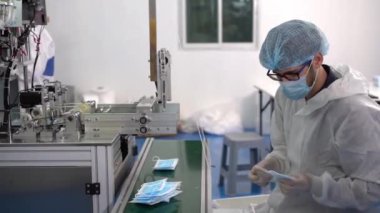 Bir maske fabrikasındaki işçiler modern bir fabrikadaki ürünün kalitesini inceliyorlar..