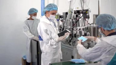 Bir maske fabrikasında çalışanlar modern endüstriyel makinelerdeki ürünlerin kalitesini kontrol ediyorlar..