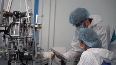 Maske fabrikasındaki çalışanlar ve çalışanlar makineyi çalıştırmak için Tablet girişini kullanıyorlar. Bir maske fabrikasında çalışanlar modern endüstriyel makinelerdeki ürünlerin kalitesini kontrol ediyorlar..