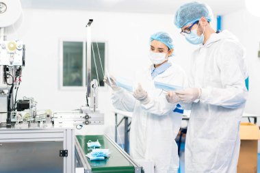 Bir maske fabrikasında çalışanlar modern endüstriyel makinelerdeki ürünlerin kalitesini kontrol ediyorlar. Toz ve Virüs Maskesi Fabrikası