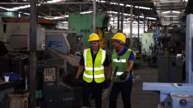 Mühendisler ve sanayi işçileri büyük makineler üzerinde çalışıyorlar. Mühendis tabletle robotu kontrol ediyor. İşi genç teknisyenler kontrol ediyor..