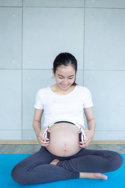 Hamile anne bebeği rahatlatmak için müzik açıyor. Karnında kulaklıkla oturan hamile bir kadın..