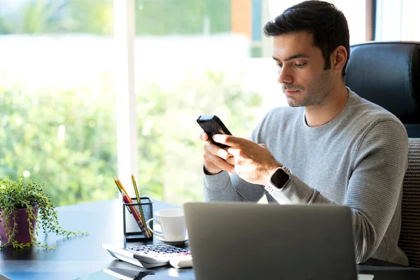 Young Businessman at home working on laptop. Man holding Mobile phone and using his mobile phone. Work from home.