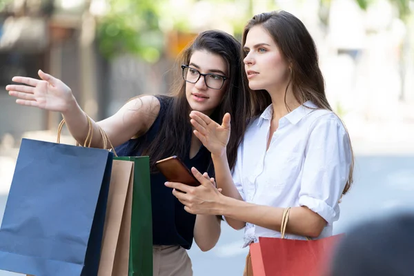 Alışveriş çantası taşıyan bir kadın şehirde cep telefonu tutan bir kadına yol tarifi veriyor. Genç ve güzel bir kadın başarılı bir alışveriş sonrası yürüyor..