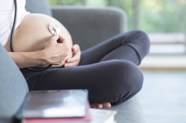 Hamile bir anne steteskopla bebeğini dinliyor. Steteskoplu hamile bir kadın karnındaki bebek kalp atışlarını dinliyor..